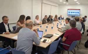 Reunión sobre transformación digital municipal Personas reunidas alrededor de una mesa mientras se muestra una presentación en una pantalla.