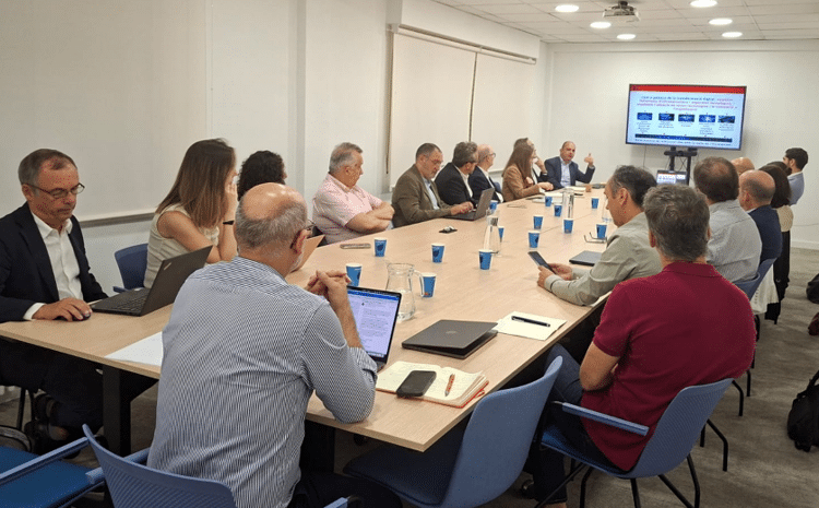 Reunión sobre transformación digital municipal Personas reunidas alrededor de una mesa mientras se muestra una presentación en una pantalla.